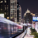 The BTS Skytrain running at night around buildings in Asoke, Bangkok.