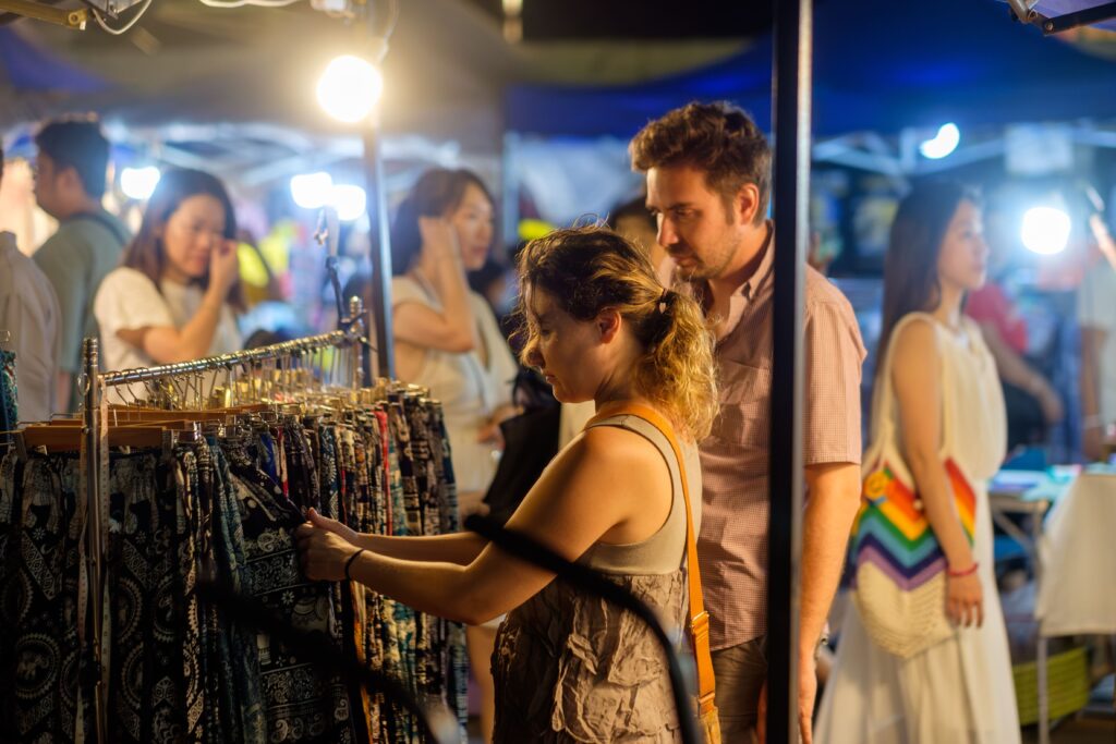 Foreigners looking at elephant pants at a market in Thailand.