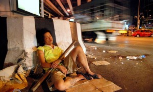 Woman asleep with a large stick in her arms beneath the Thai-Belgian bridge at Rama 4/Sathorn/Wireless road intersection