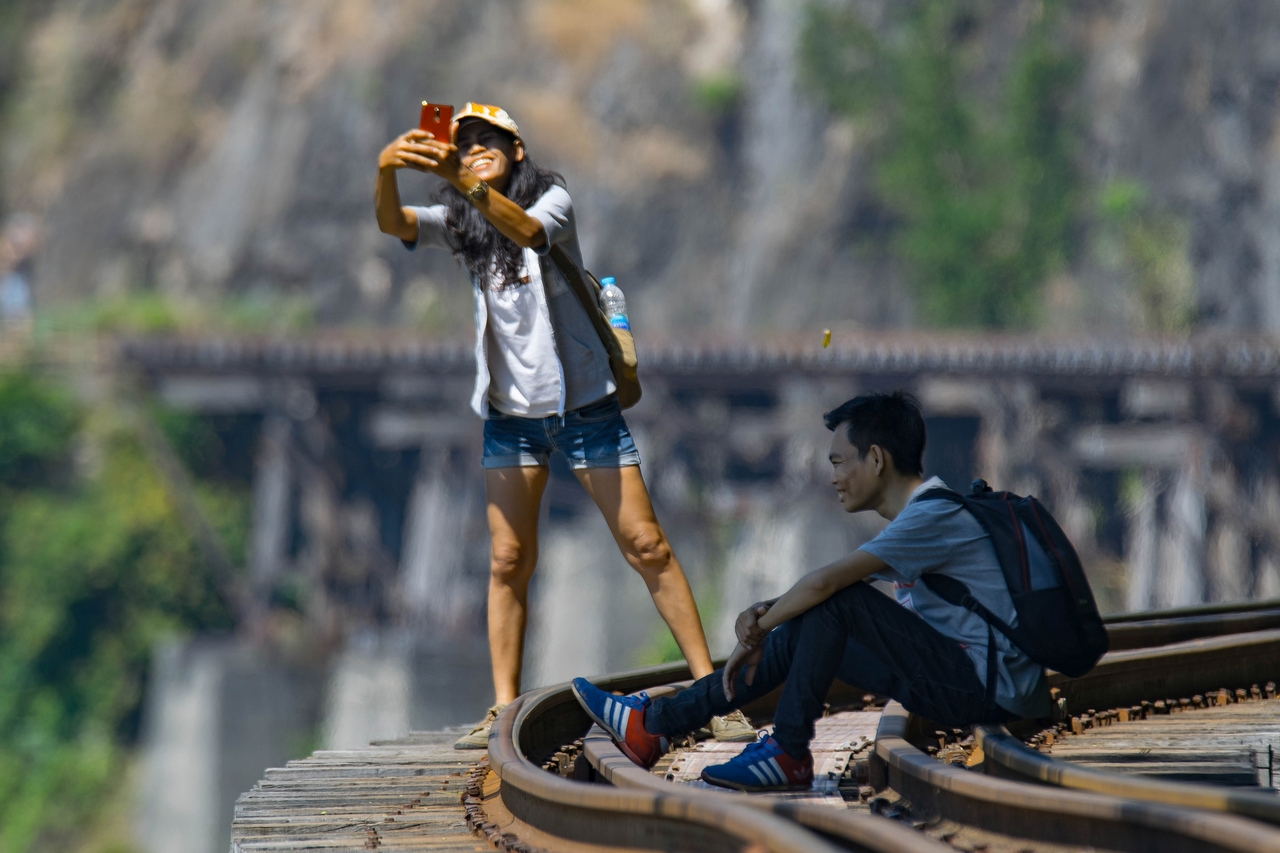 Tourists take smiling selfies on Death Railway, on the famous River Kwai Bridge in Kanchanaburi