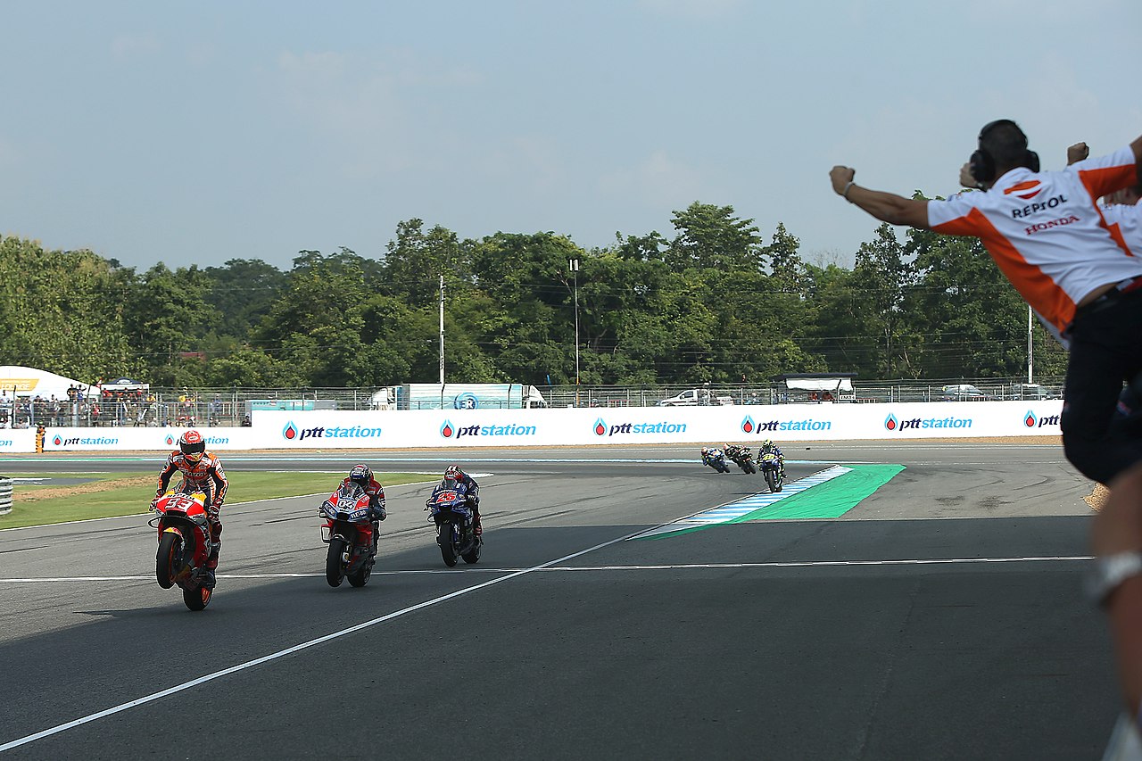Marc Márquez, riding his Repsol Honda, doing a wheelie whilst crossing the line and winning the 2018 MotoGP Grand Prix in Buri Ram.