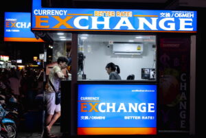 Man in gray short standing in front a counter of currency exchange.
