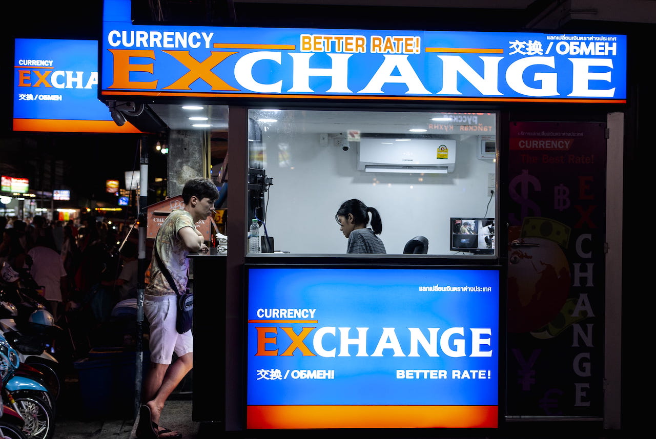 Man in gray short standing in front a counter of currency exchange.