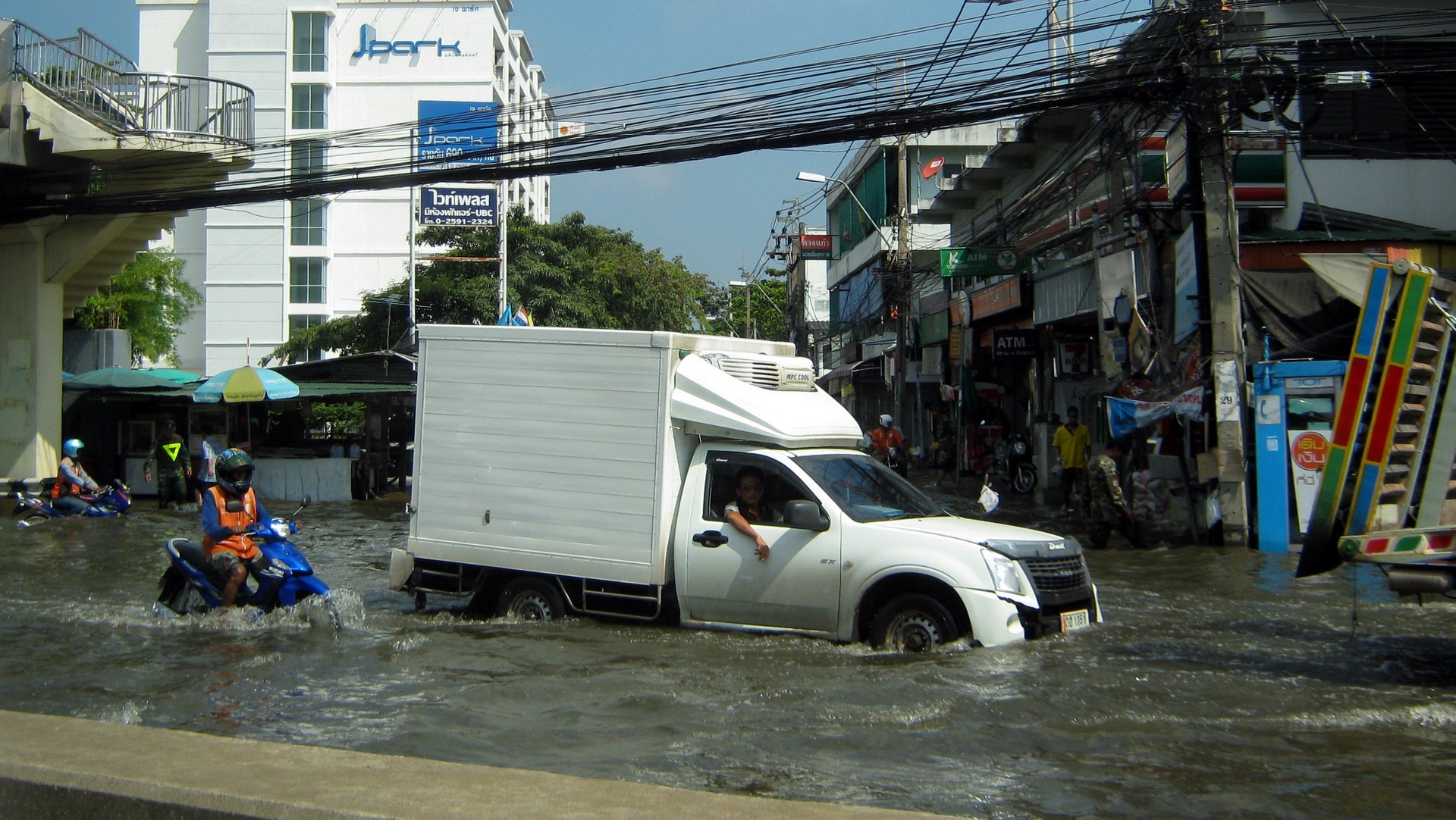 A pickup truck and a motorcycle driving through a flooded street in Bangkok