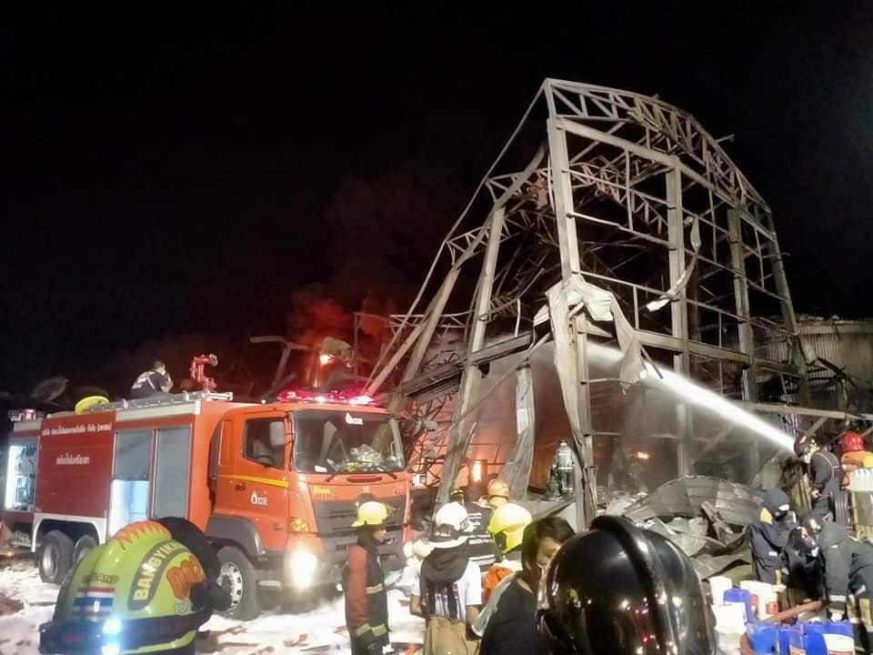 Firefighters spray foam amid twisted metal frames of a charred chemical factory in Samut Prakan
