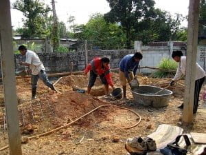 Workers mixing concrete in a tub and pouring it with buckets in Trat Province