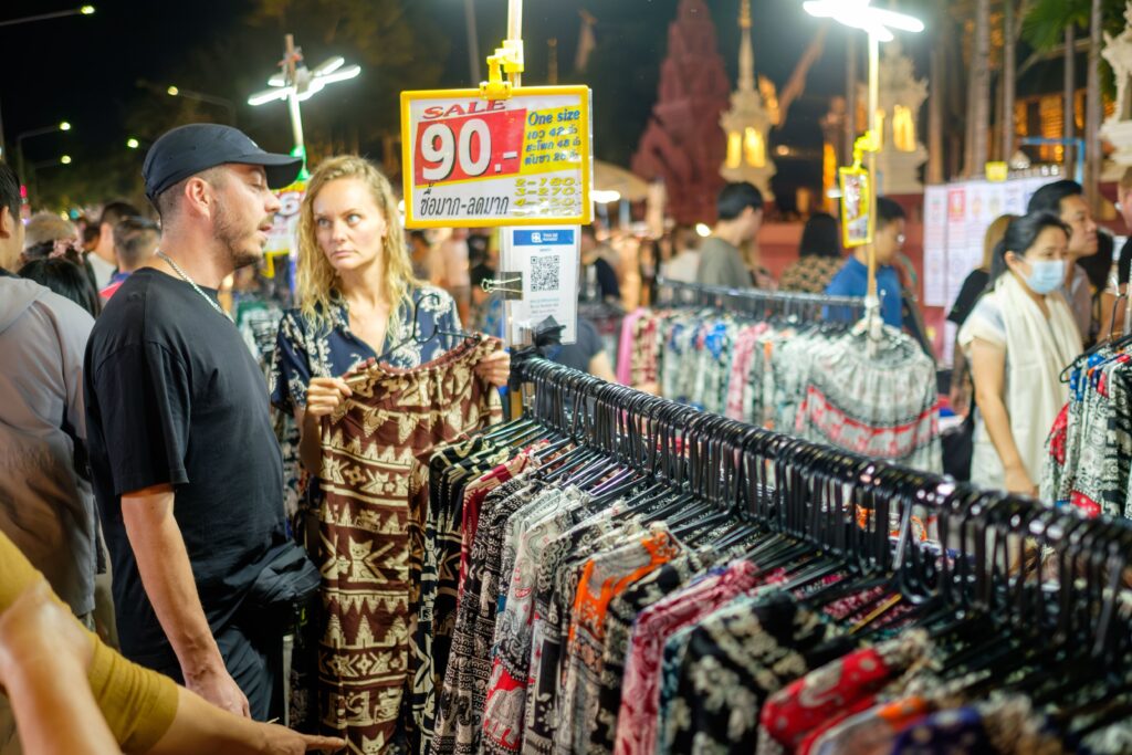 Tourists looking at elephant pants at a market in Thailand.