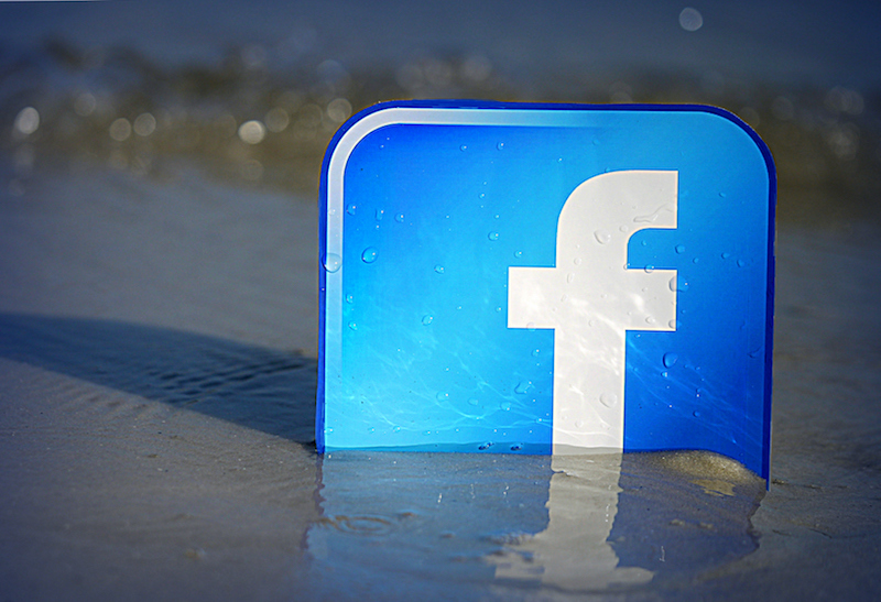 Facebook logo semi buried in beach sand