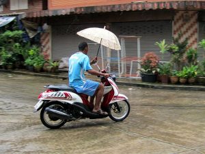 Thai man riding a Yamaha Mio Fino Sport scooter and holding an umbrella