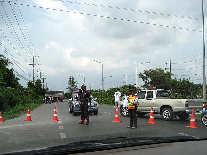 Thai police officer controlling bypassing traffic at the scene of a road accident involving a truck on Bang Na